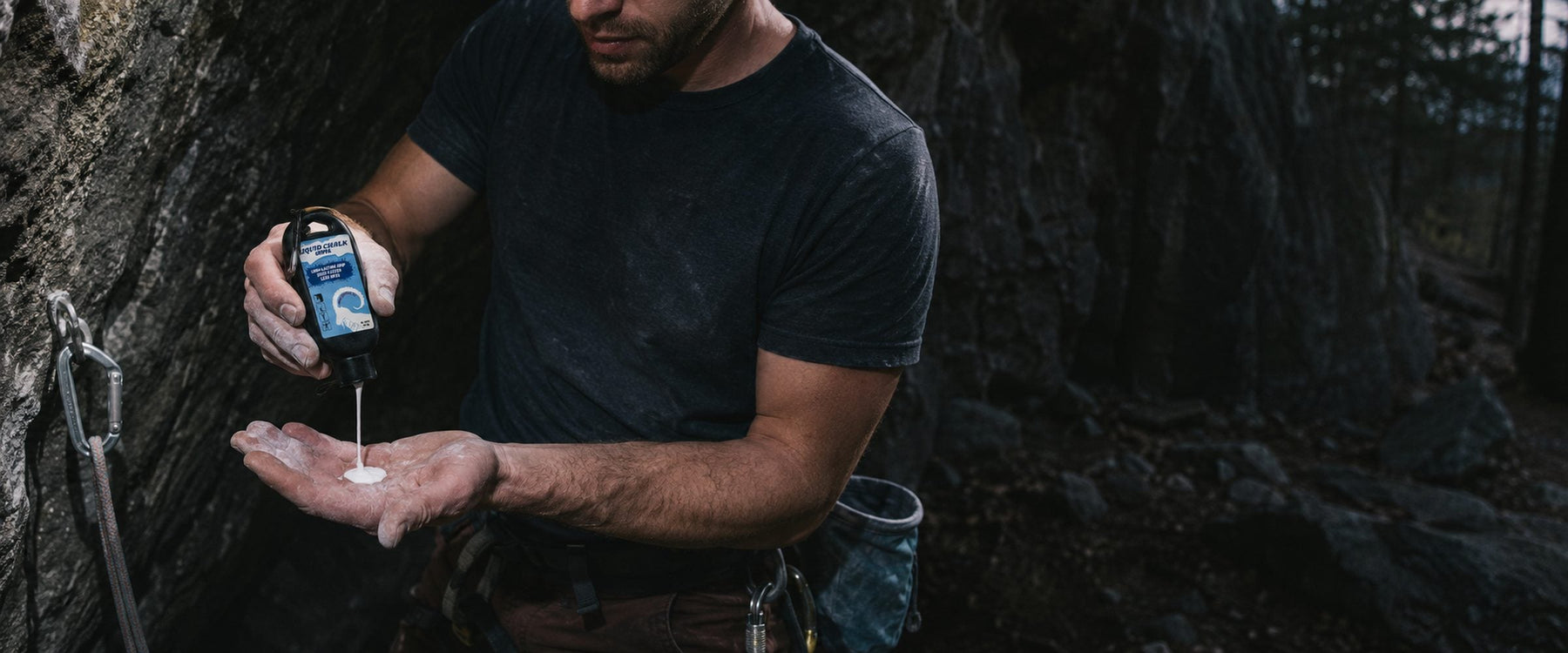 Climber squeezing Grippa liquid chalk into an open palm at the base of a crag