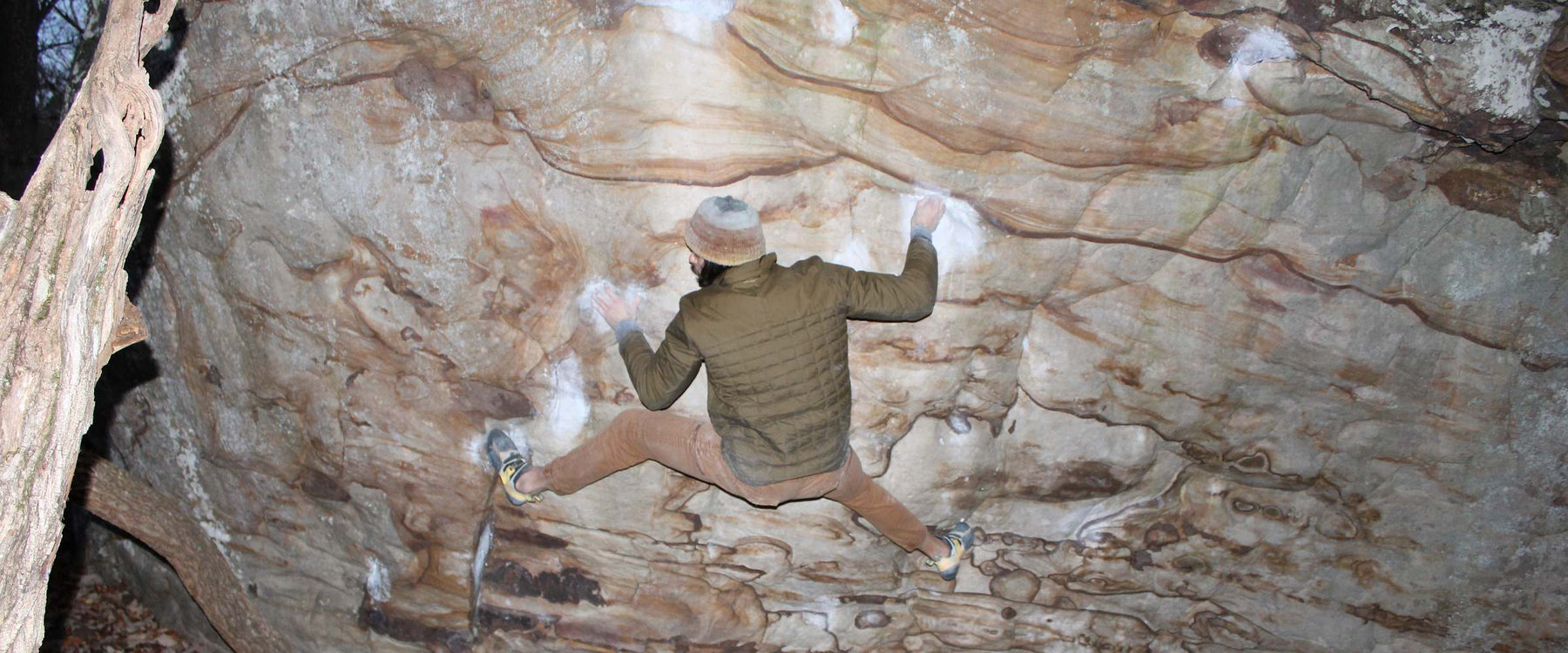 Climber spread wide across a chalked sandstone roof, mid-move on an overhanging boulder problem