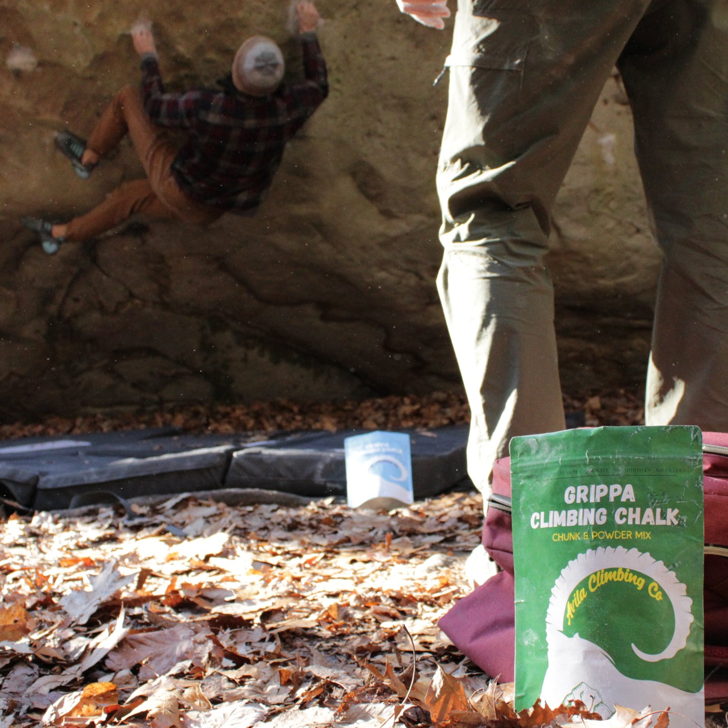 Person climbing a rock wall with a package of Grippa climbing chalk on the ground.